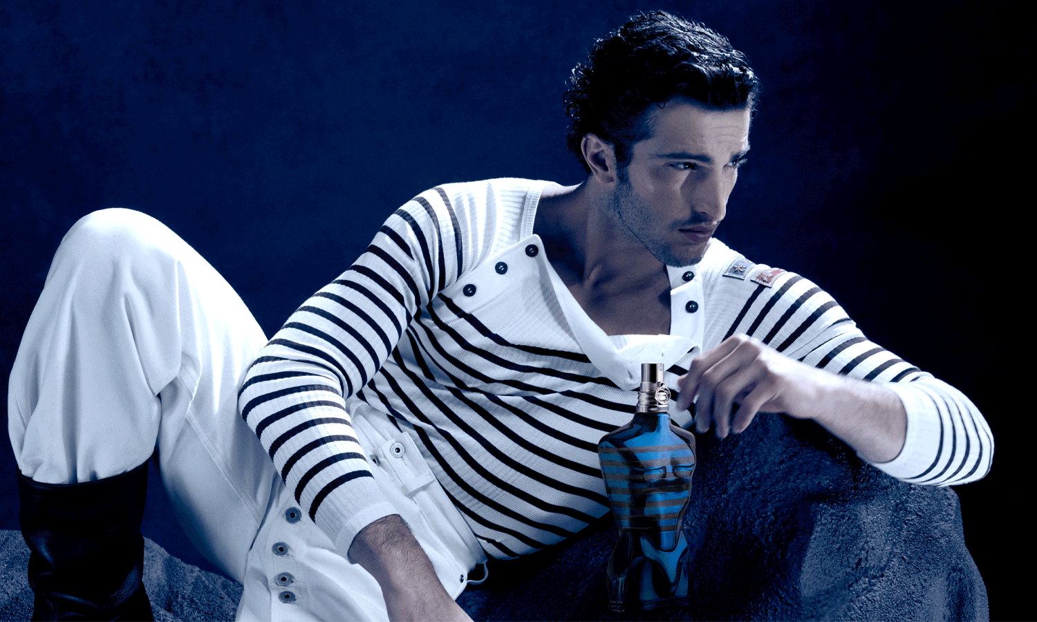 A man in a striped jersey lying on a black rock with Le Male In Blue